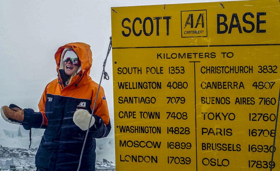 Journalistin Ashlan Gorse Cousteau posiert beim Scott Base Schild in der Antarktis. Das gelbe Schild, im Stil der neuseelÃ¤ndischen Automobile Association, zeigt Entfernungen von Scott Base zu verschiedenen StÃ¤dten der Welt an. Von hier sind es noch 1353 km bis zum SÃ¼dpol.